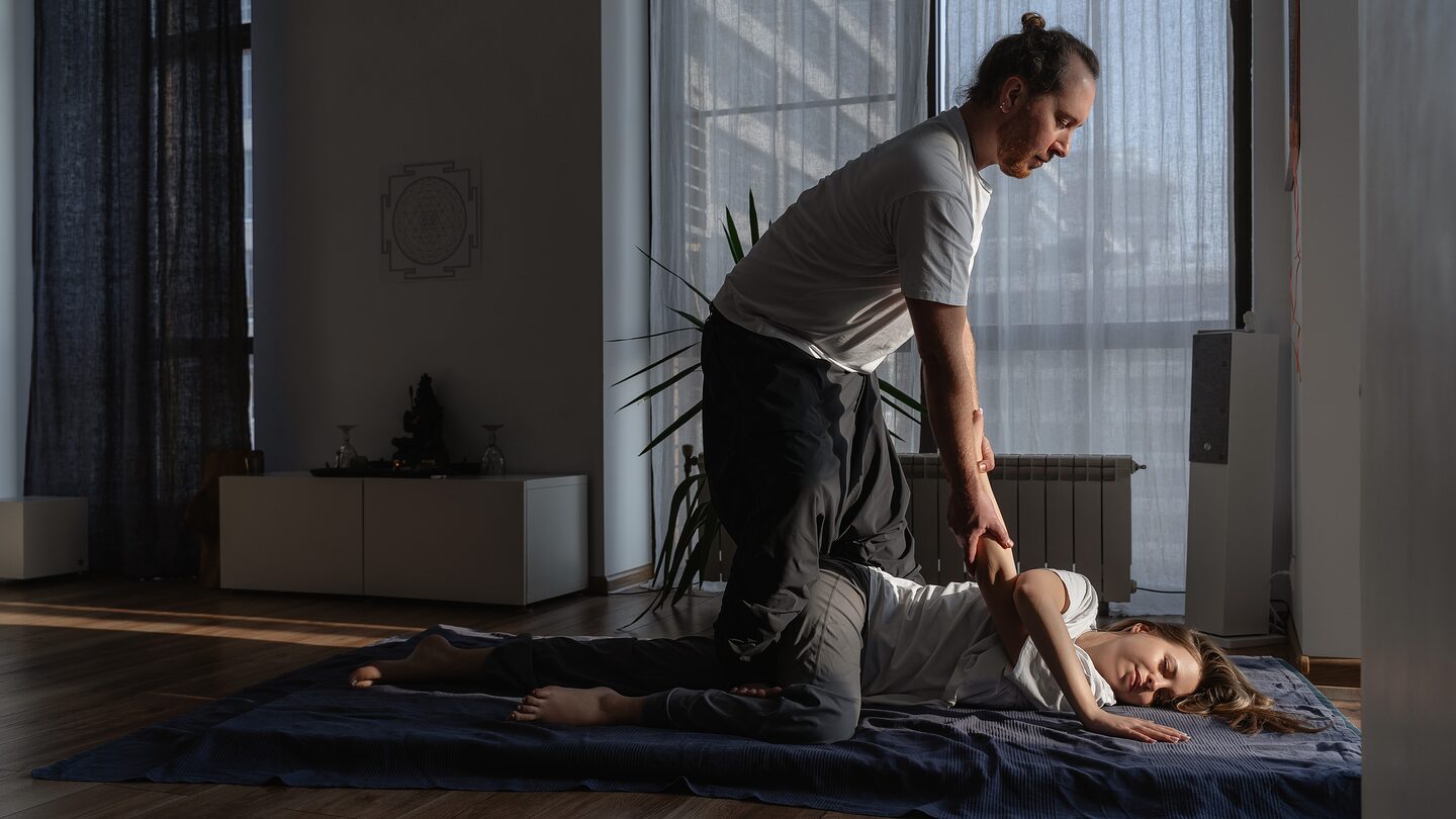 йога-массаж в Казани — мастер выполняет пассивную растяжку ног клиента на мате